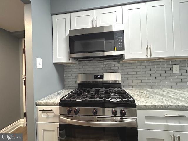 kitchen featuring decorative backsplash, appliances with stainless steel finishes, white cabinetry, and light stone counters