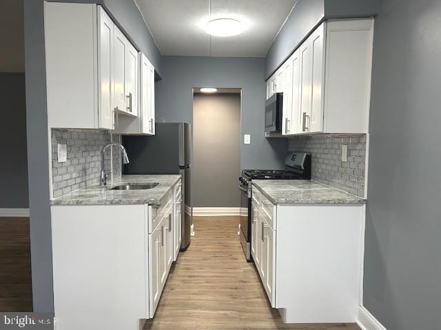 kitchen featuring gas stove, light stone counters, sink, and white cabinets