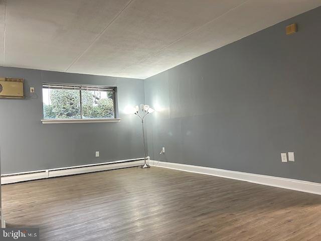 unfurnished room featuring hardwood / wood-style flooring and a baseboard heating unit