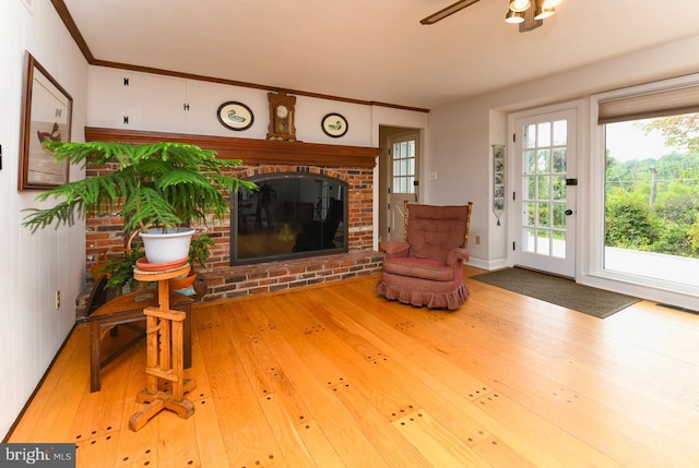 unfurnished living room featuring wood-type flooring, a brick fireplace, ceiling fan, and ornamental molding