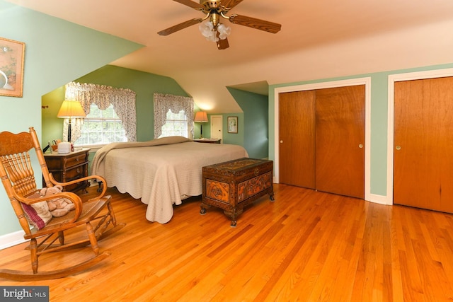 bedroom featuring vaulted ceiling, ceiling fan, light hardwood / wood-style flooring, and two closets