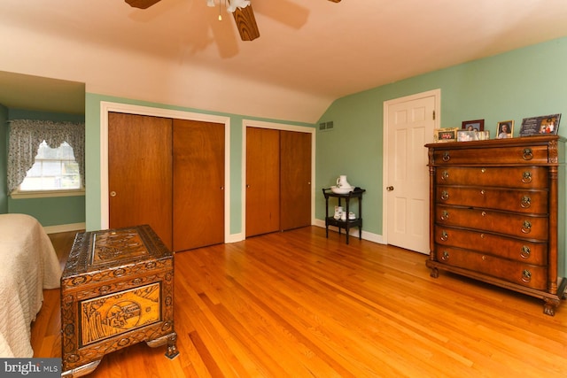 bedroom with two closets, vaulted ceiling, ceiling fan, and hardwood / wood-style flooring