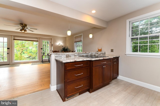 kitchen with ceiling fan, light stone counters, kitchen peninsula, decorative light fixtures, and black electric stovetop