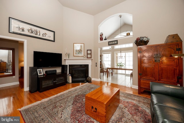 living room featuring a high ceiling, a premium fireplace, a chandelier, and light hardwood / wood-style flooring