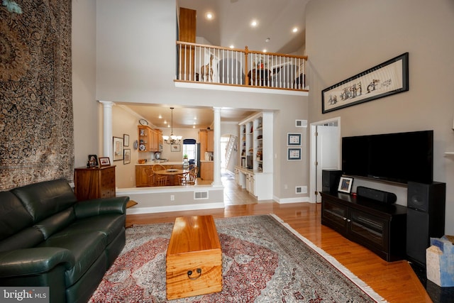 living room featuring crown molding, decorative columns, a high ceiling, light hardwood / wood-style floors, and a chandelier