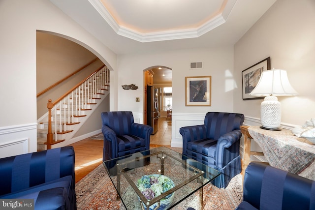 living room with crown molding, a tray ceiling, and wood-type flooring