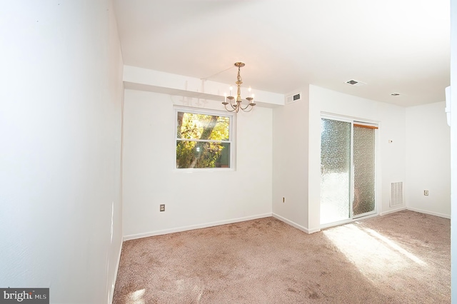 carpeted spare room featuring an inviting chandelier