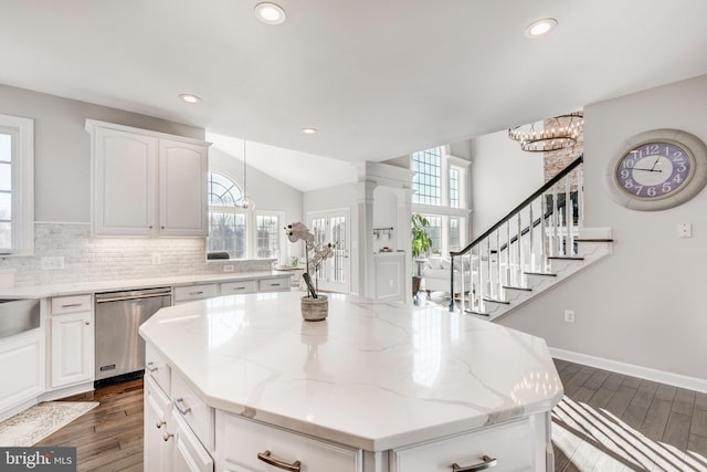 kitchen featuring a kitchen island, light stone countertops, stainless steel dishwasher, and white cabinetry