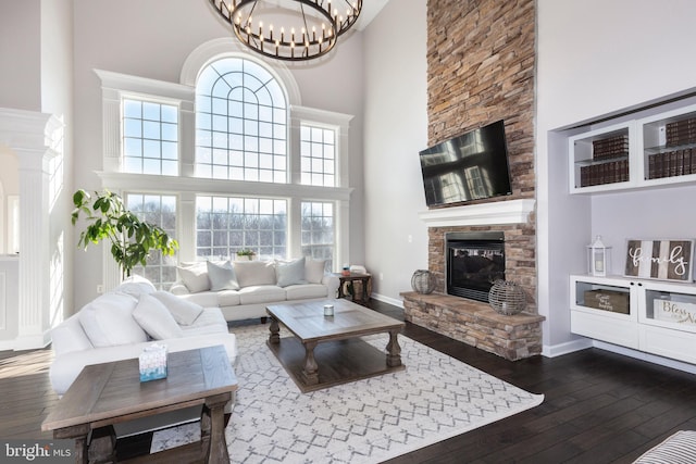 living room featuring a towering ceiling, dark wood-type flooring, a notable chandelier, and a stone fireplace