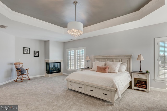 carpeted bedroom with ornamental molding, a multi sided fireplace, a raised ceiling, and a chandelier