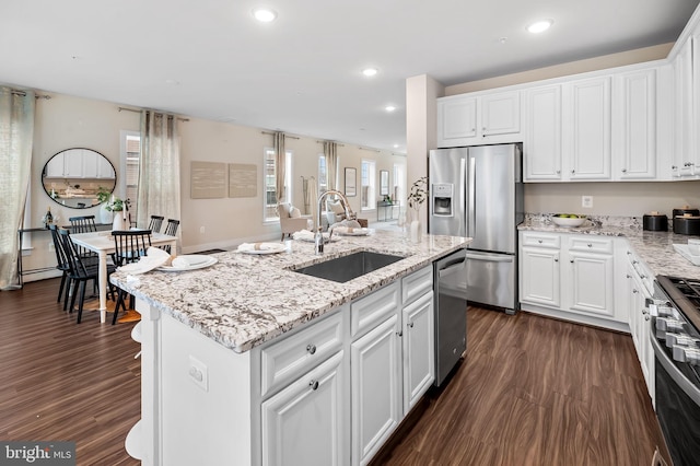 kitchen with stainless steel appliances, sink, white cabinets, dark hardwood / wood-style floors, and an island with sink