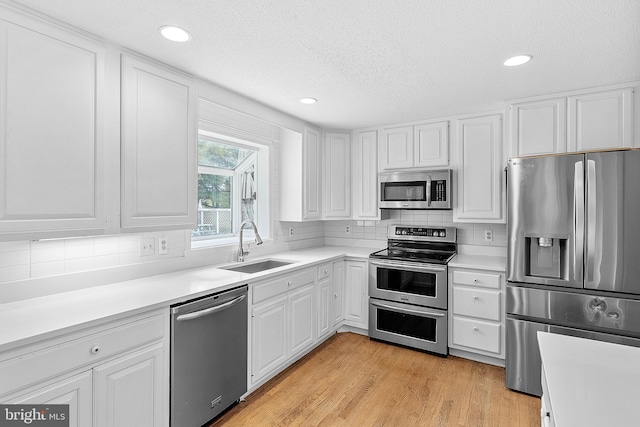 kitchen with sink, white cabinets, stainless steel appliances, and light hardwood / wood-style flooring