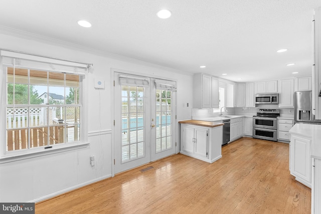 kitchen featuring french doors, light hardwood / wood-style floors, a healthy amount of sunlight, white cabinetry, and stainless steel appliances