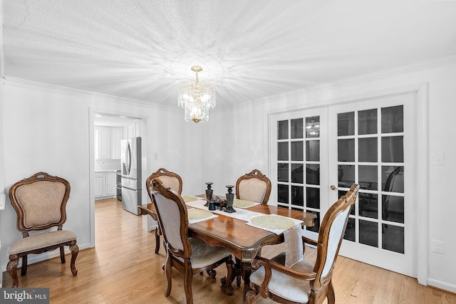 dining area with light wood-type flooring, french doors, crown molding, and an inviting chandelier