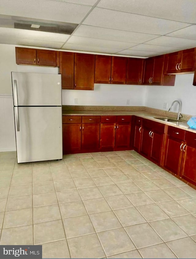 kitchen with stainless steel fridge, a paneled ceiling, light tile patterned floors, and sink