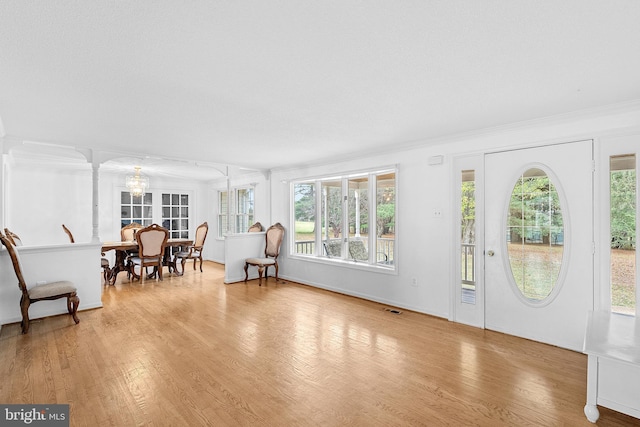 interior space featuring a notable chandelier, a healthy amount of sunlight, light wood-type flooring, and ornamental molding