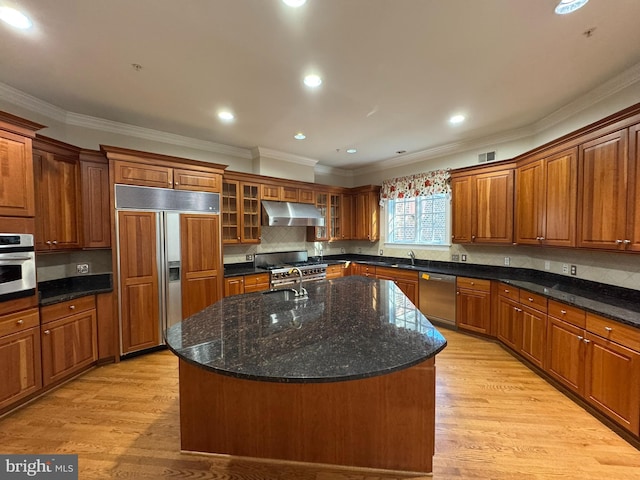 kitchen featuring dark stone countertops, backsplash, premium appliances, an island with sink, and light wood-type flooring