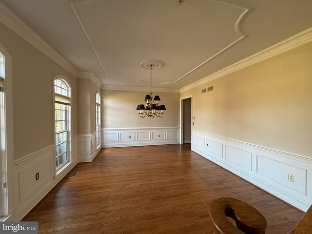 unfurnished dining area featuring dark wood-type flooring, ornamental molding, and a chandelier