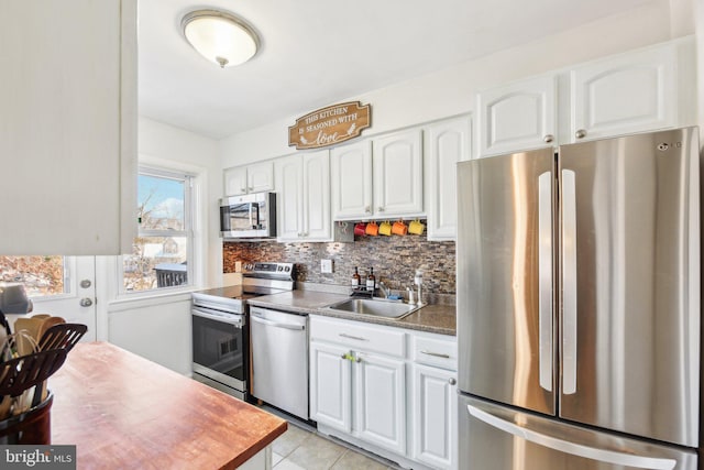 kitchen featuring appliances with stainless steel finishes, tasteful backsplash, sink, light tile patterned floors, and white cabinetry