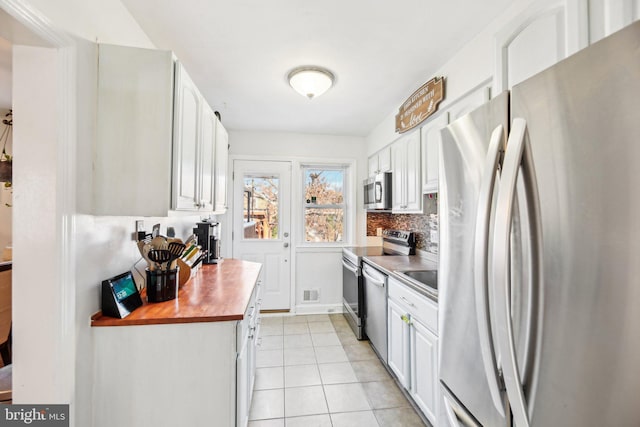 kitchen with backsplash, stainless steel appliances, white cabinets, butcher block countertops, and light tile patterned flooring