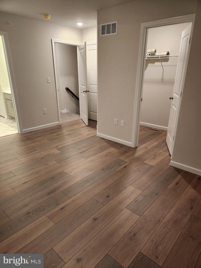 unfurnished bedroom with a spacious closet, a closet, and wood-type flooring