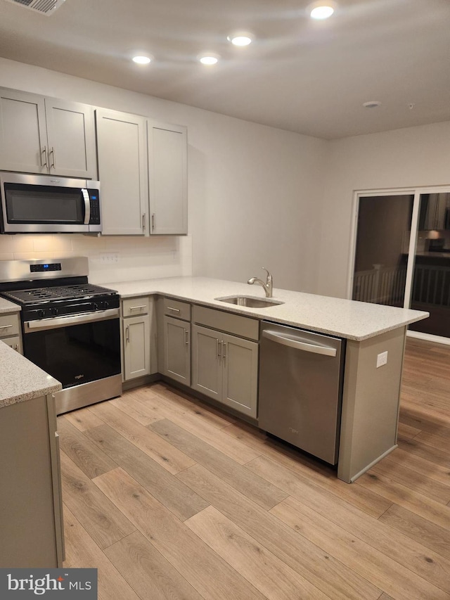 kitchen featuring kitchen peninsula, stainless steel appliances, light hardwood / wood-style floors, and sink