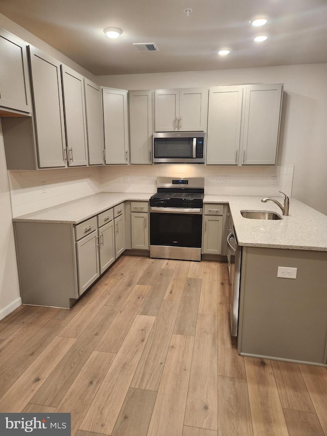 kitchen featuring appliances with stainless steel finishes, light wood-type flooring, light stone counters, sink, and gray cabinets