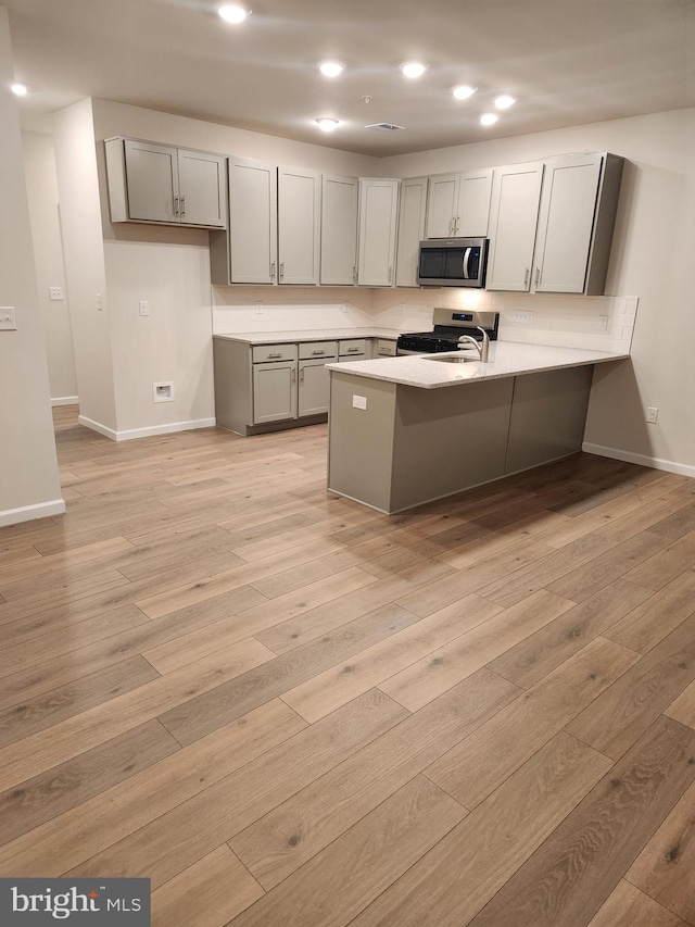 kitchen with stainless steel appliances, a kitchen breakfast bar, light hardwood / wood-style flooring, kitchen peninsula, and gray cabinets