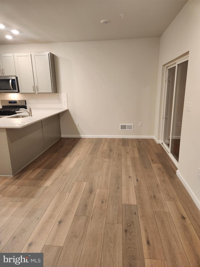 kitchen with kitchen peninsula, white cabinetry, light wood-type flooring, and appliances with stainless steel finishes