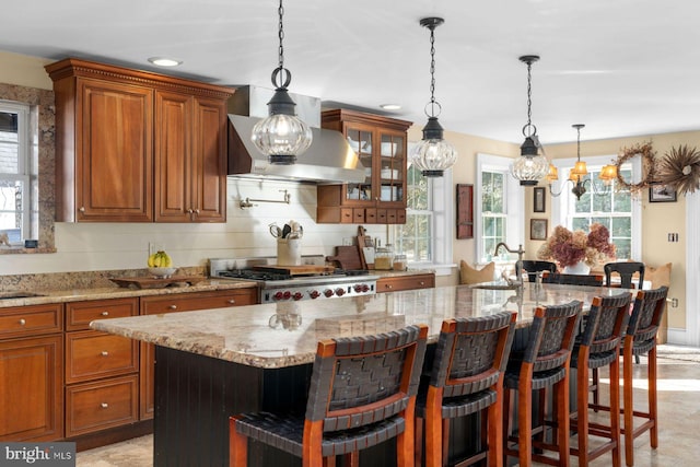 kitchen with light stone counters, a breakfast bar area, an island with sink, and wall chimney exhaust hood