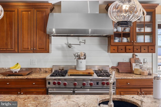 kitchen featuring double oven range, wall chimney range hood, and light stone counters