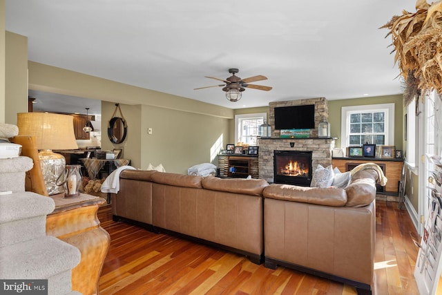 living room with ceiling fan, wood-type flooring, and a stone fireplace