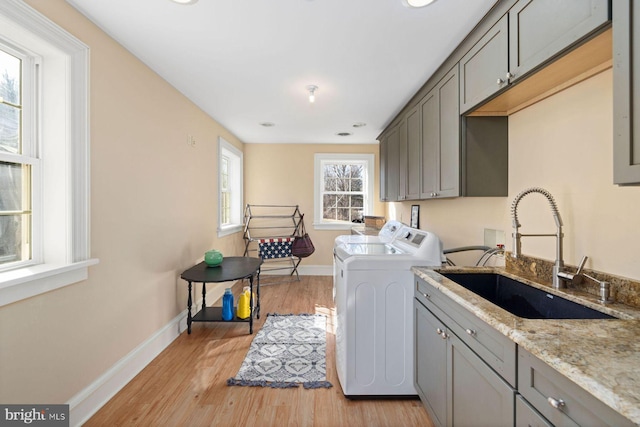 washroom featuring cabinets, sink, washing machine and dryer, and light hardwood / wood-style flooring