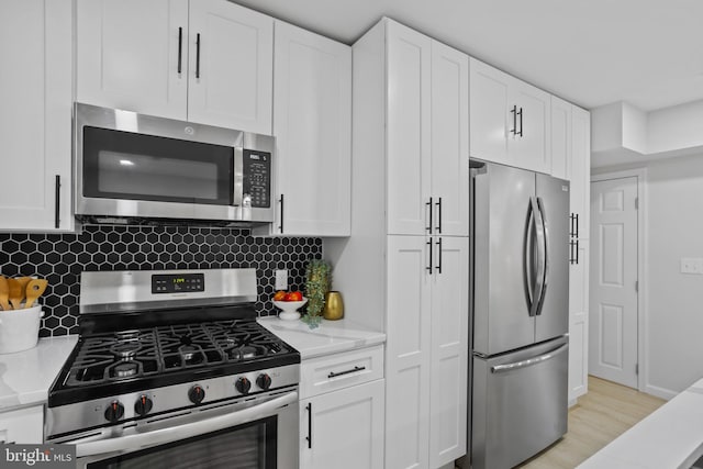 kitchen with light stone countertops, tasteful backsplash, stainless steel appliances, white cabinets, and light hardwood / wood-style floors