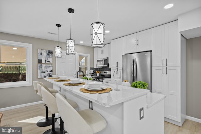 kitchen with pendant lighting, light stone countertops, an island with sink, white cabinetry, and stainless steel appliances