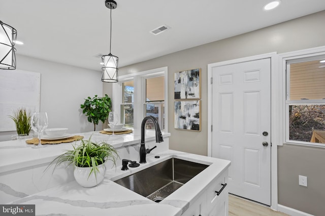 kitchen featuring sink, light stone counters, light hardwood / wood-style flooring, pendant lighting, and white cabinets