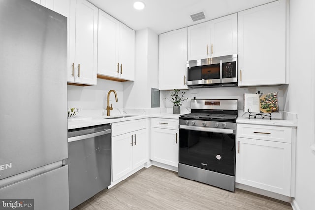 kitchen with stainless steel appliances, white cabinetry, sink, and light hardwood / wood-style flooring