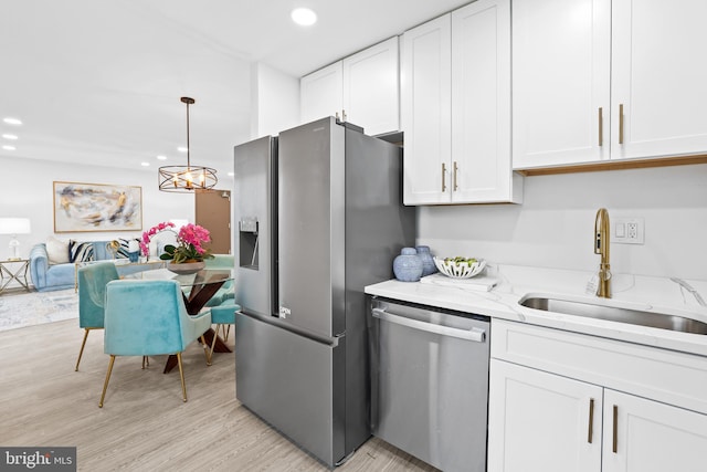 kitchen with sink, white cabinetry, hanging light fixtures, appliances with stainless steel finishes, and light stone countertops