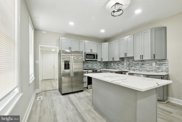 kitchen with light stone countertops, a center island, sink, gray cabinets, and appliances with stainless steel finishes