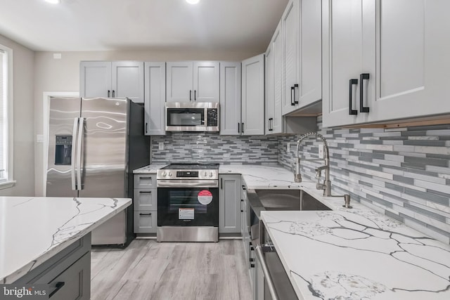 kitchen with light stone countertops, gray cabinets, decorative backsplash, and stainless steel appliances