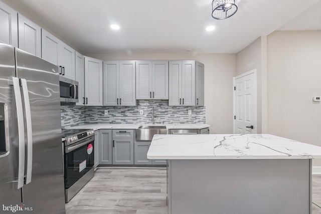 kitchen featuring gray cabinetry, light stone countertops, a kitchen island, and appliances with stainless steel finishes