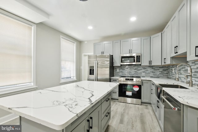 kitchen featuring backsplash, light stone countertops, sink, and appliances with stainless steel finishes