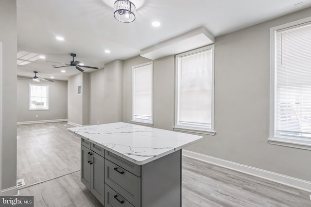 kitchen with light stone counters, ceiling fan, gray cabinets, a center island, and light hardwood / wood-style floors