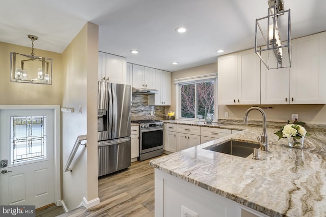 kitchen featuring sink, white cabinetry, light stone counters, decorative light fixtures, and appliances with stainless steel finishes