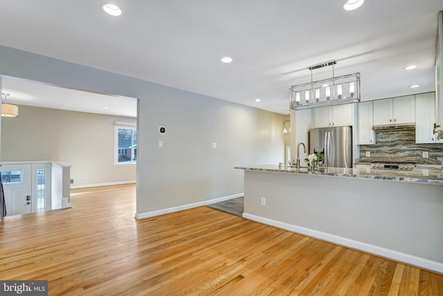 kitchen with pendant lighting, white cabinetry, stainless steel refrigerator with ice dispenser, light stone counters, and tasteful backsplash