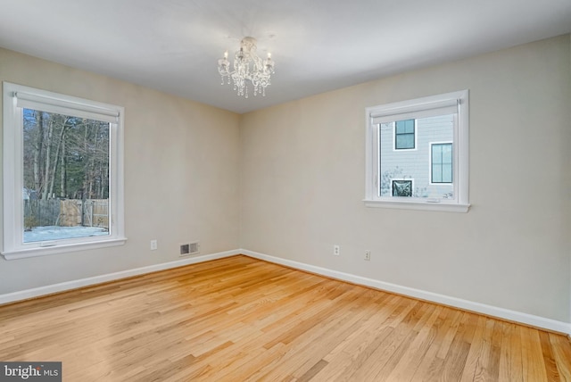 spare room featuring a notable chandelier and light hardwood / wood-style floors