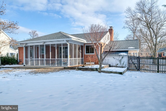 snow covered back of property with a sunroom