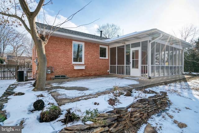 snow covered back of property featuring central AC and a sunroom