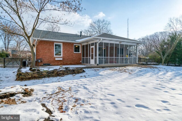 snow covered back of property with a sunroom