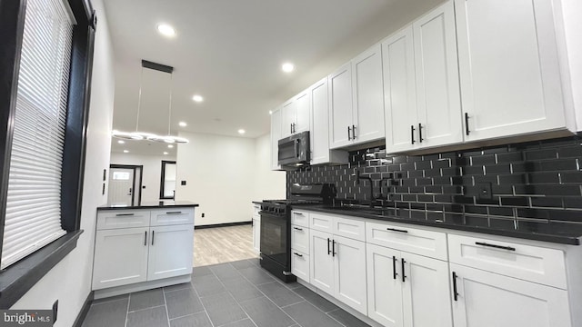 kitchen featuring pendant lighting, black gas range, white cabinets, dark tile patterned flooring, and sink